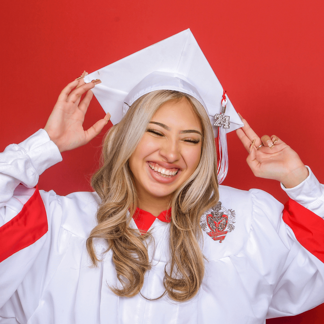 Woman in a white cap and gown on a red background posing for graduation pictures.