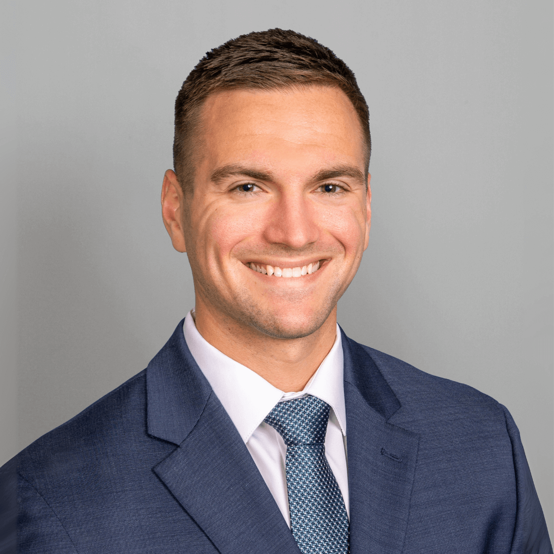 Man in a suit and tie posing for business headshots on a gray background.