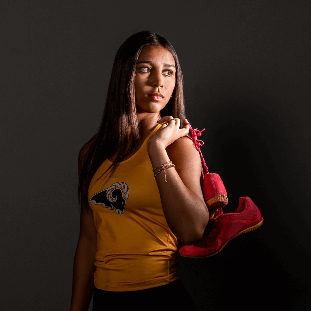 Woman wearing a track uniform and holding her shoes, posing for senior pictures.