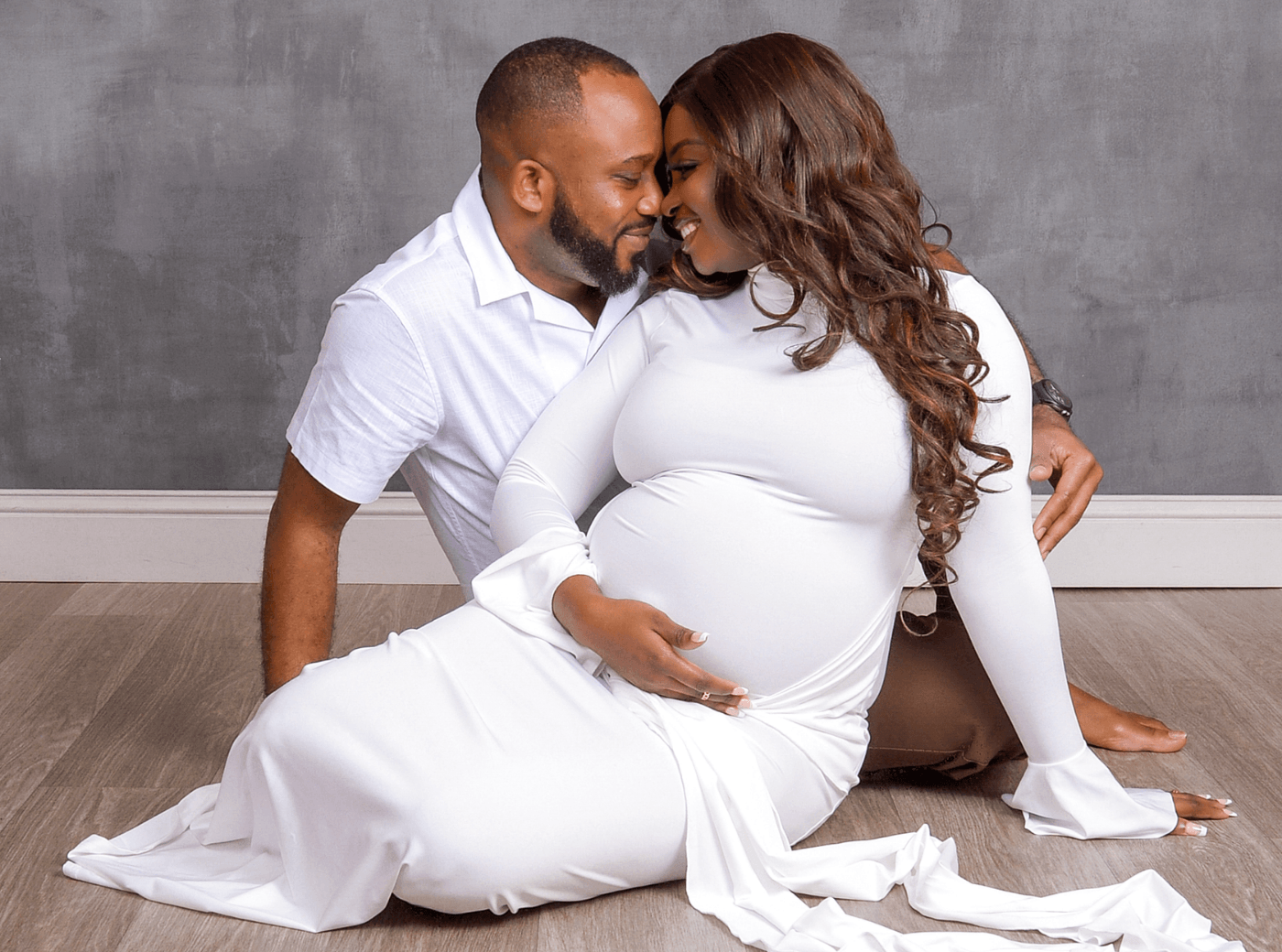 Couple in white outfits posing on the floor for professional maternity pictures.